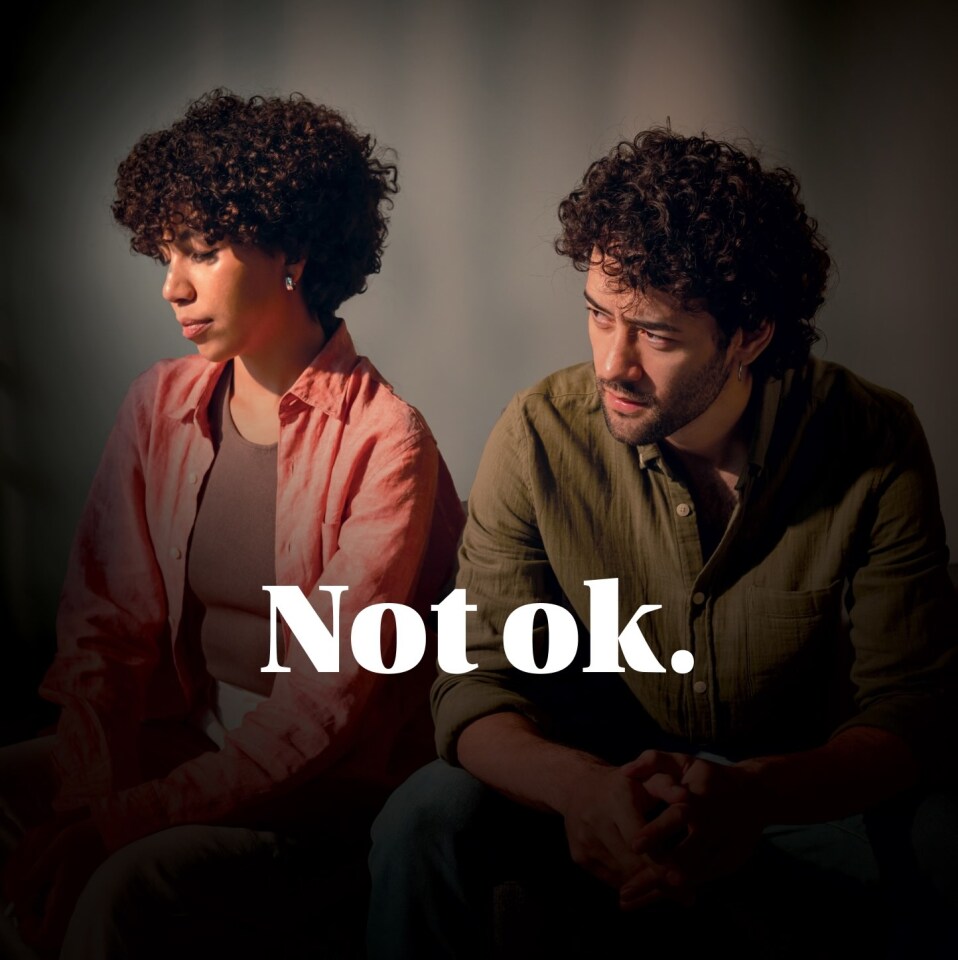 Two people sitting side by side in soft lighting with the words Not ok. over the image, part of the Optimism Place campaign designed by Intent.