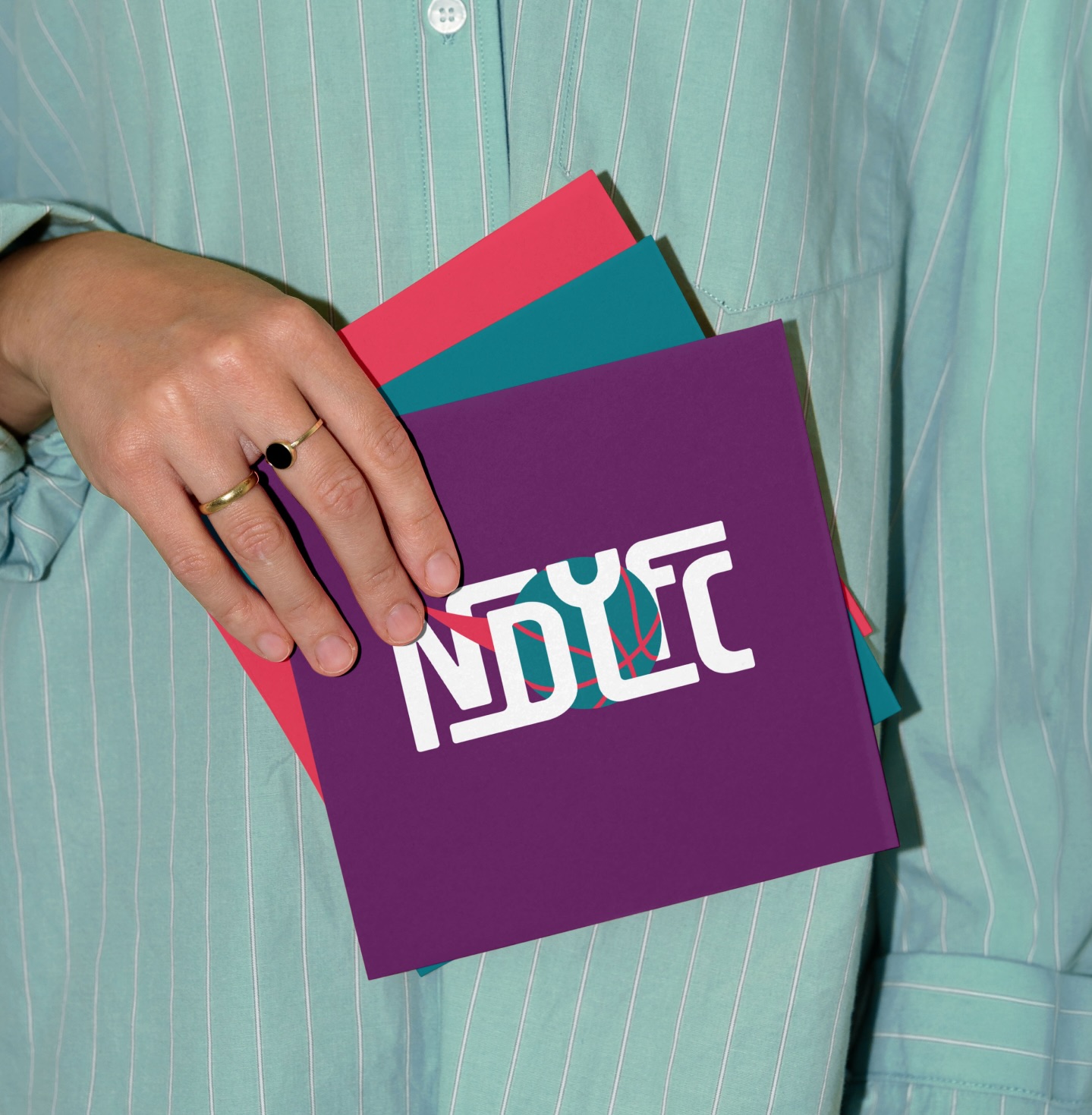 Person holding a collection of colourful New Dawn Youth and Family Centre branded cards in purple, teal, and pink, featuring the NDYFC logo.
